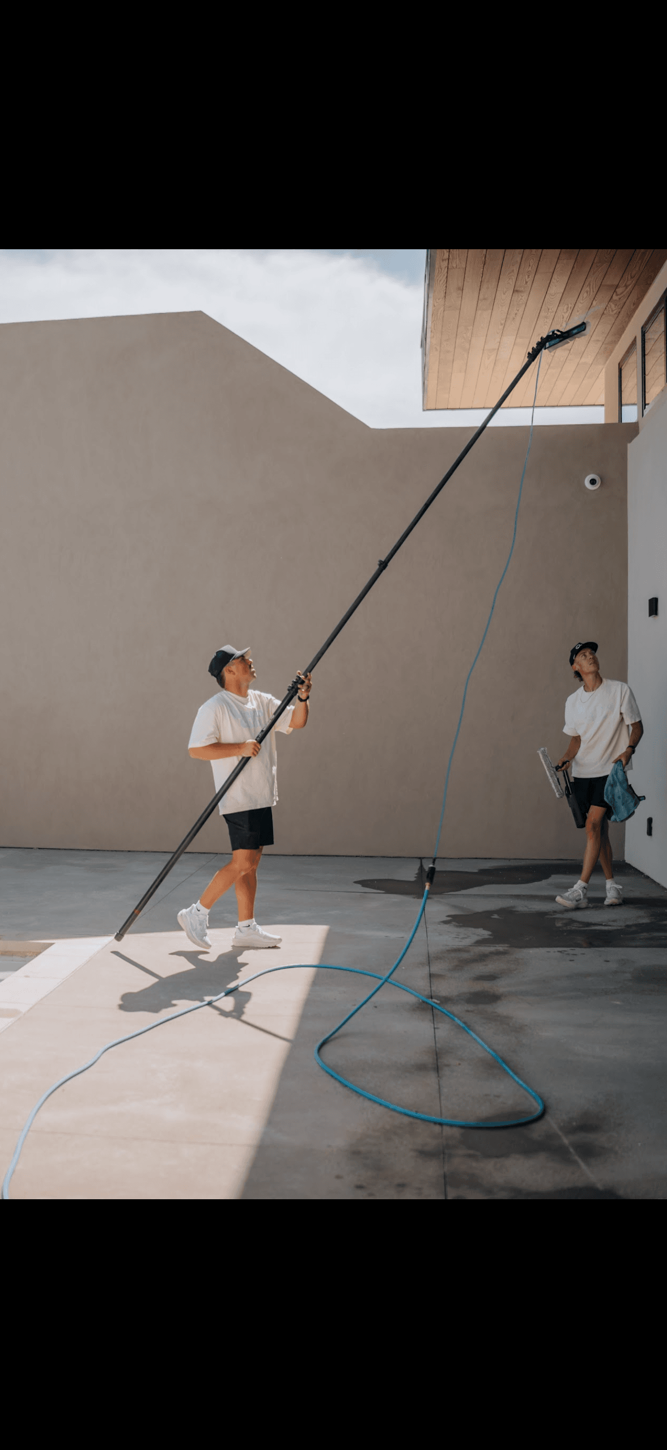 Action shot of two employees cleaning exterior of window with water pole